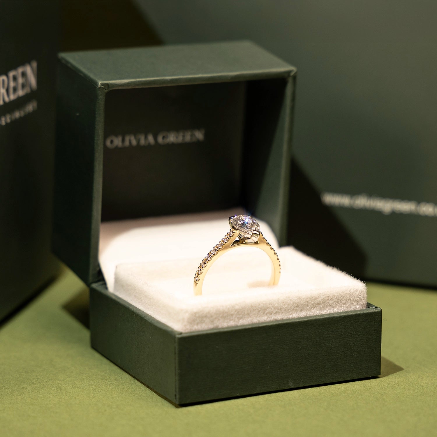 Gold ring in a black Olivia Green box on a green surface